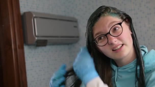 Uma rapariga milenar pinta o cabelo louro de azul em casa na casa de banho. Home cuidado do cabelo durante a carantina de coronavírus . — Vídeo de Stock