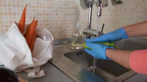 医療用手袋を身に着けている女性の手のクローズアップは Covid 19から身を守るためにコロナウイルスの流行の間 彼女の台所で自宅でズッキーニを洗っています 隔離封鎖における自己分離 — ストック動画