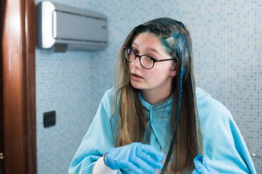 Bin yıllık bir kız, sarı saçlarını evinde, banyoda, aynaya bakarak maviye boyar. Koronavirüs karantinası sırasında ev yapımı saç bakımı. Bu onun için zor, o kızgın, başarılı olamıyor.