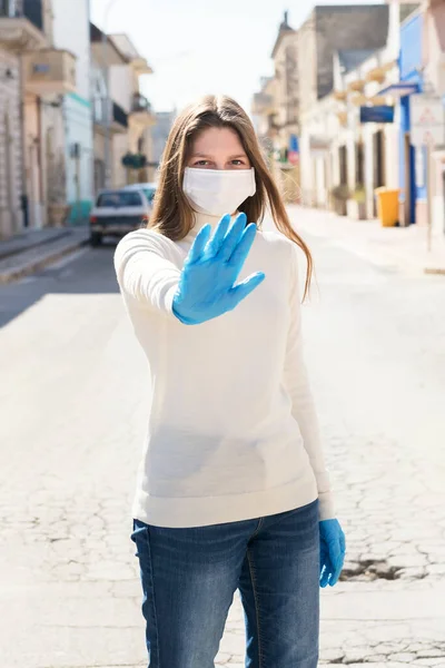 A millennial girl wearing face protection mask and gesturing stop by gloved hand, coronavirus prevention and social distancing concept