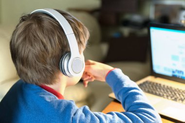 Masada dizüstü bilgisayarla oturan kulaklıklı sarışın çocuğun kafasını kapat. Evde eğitim ve öğretim evden internet üzerinden