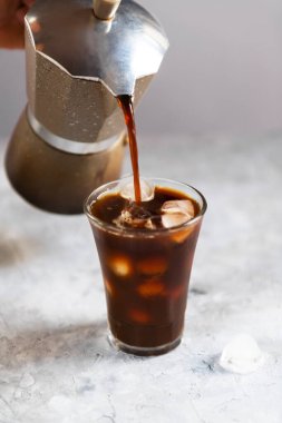 Taze kahve mocha 'dan koyu gri arka planda buzla kaplı uzun bir bardağa dökülüyor, yakın plan. Buzlu yaz kahvesi konsepti, kapat.