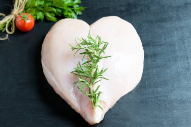 Çiğ kalp şeklinde tavuk göğsü, marul yaprakları üzerinde. Sağlıklı beslenme konsepti. Siyah arka planda spor beslenme ve proteinler, üst görünüm