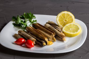 Gri arka planda beyaz bir tabakta otlu ve limonlu taze deniz ürünleri. Yiyecek çerçevesi.