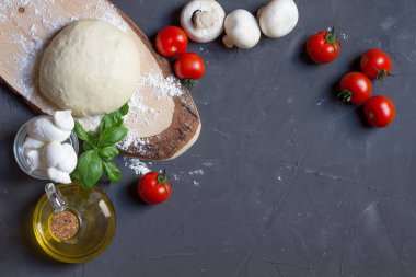 Çiğ pizza malzemeleri: domates, mozzarella, fesleğen, hamurun ortasında fotokopi alanı olan gri tahta.