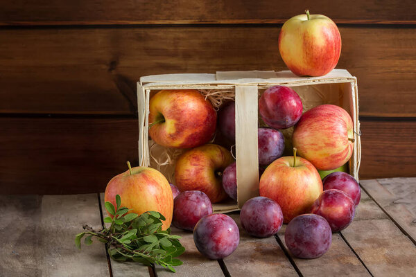 Gifts of autumn: apples and plums in a basket on a wooden background, autumn composition, harvest, horyzontal