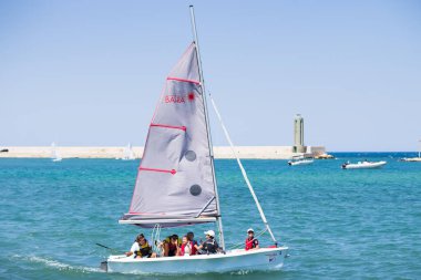 BARI, İtalya - 11 Temmuz 2018, deniz manzaralı yeşil deniz feneri ve güneş, Apulia, İtalya 'ya demir atan insanlarla dolu bir motorlu tekne