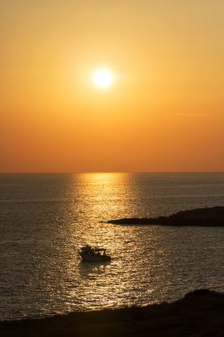 Adriyatik Denizi 'nde Salento' da güzel bir gün batımı, güneş yolunda sallanan küçük bir tekne, yanlarda bulanık manzaralı gölgeler, Apulia, güney İtalya