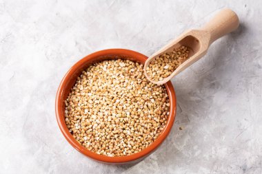 Kahverengi bir kasede çiğ yeşil karabuğday ve gri arka planda ahşap bir kepçe. Kızarmamış organik çiğ vejetaryen yiyeceği öğütüyor. Sağlıklı ve dengeli bir diyet, kilo kaybı, üst görünüm