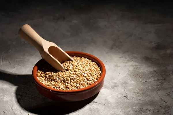 Kahverengi bir kasede çiğ yeşil karabuğday ve gri arka planda ahşap bir kepçe. Kızarmamış organik çiğ vejetaryen yiyeceği öğütüyor. Sağlıklı ve dengeli bir diyet, kilo kaybı