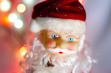 Oyuncak, heykelcik, Noel Baba. Oyuncak Noel Baba arka planda çelenk ışıkları. Face, Noel Baba 'nın vücudunun parçaları. Makroda yeni yıl oyuncağı. Takım elbise kırmızı, büyük gri beyaz bir sakal..
