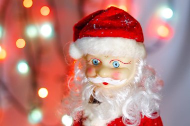 Oyuncak, heykelcik, Noel Baba. Oyuncak Noel Baba arka planda çelenk ışıkları. Face, Noel Baba 'nın vücudunun parçaları. Makroda yeni yıl oyuncağı. Takım elbise kırmızı, büyük gri beyaz bir sakal..