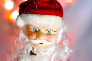 Oyuncak, heykelcik, Noel Baba. Oyuncak Noel Baba arka planda çelenk ışıkları. Face, Noel Baba 'nın vücudunun parçaları. Makroda yeni yıl oyuncağı. Takım elbise kırmızı, büyük gri beyaz bir sakal..