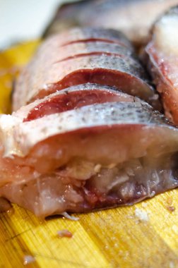 Parçalar, tahta bir tahtanın üzerinde doğranmış çiğ balık. Makrodaki balıklar. Tuzdaki balık. Balıklarda solucanlar. Balık zehirlenmesi tehlikesi.