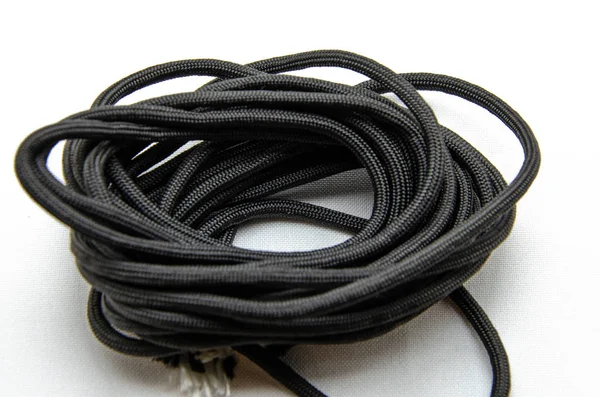 Corda Paracord. Paracord para tecelagem e turismo. Corda de segurança. Paracord tático preto em um fundo branco e nas mãos — Fotografia de Stock