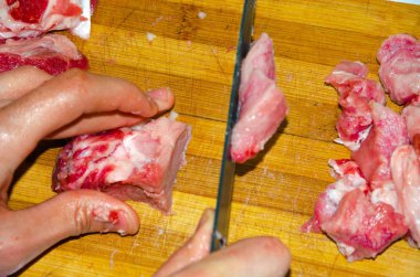 Tahtada çiğ et var. Bir adam domuz etini bıçakla parçalara ayırıyor. Pastırmalı et. Çiğ et hastalıkları. Etten yağlı eller