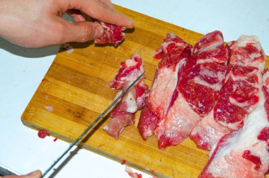 Tahtada çiğ et var. Bir adam domuz etini bıçakla parçalara ayırıyor. Pastırmalı et. Çiğ et hastalıkları. Etten yağlı eller