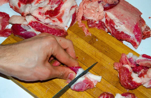 Carne cruda en el tablero. Un hombre corta carne de cerdo en pedazos con un cuchillo. Carne con tocino. Enfermedades de la carne cruda. Las manos gordas de la carne — Foto de Stock