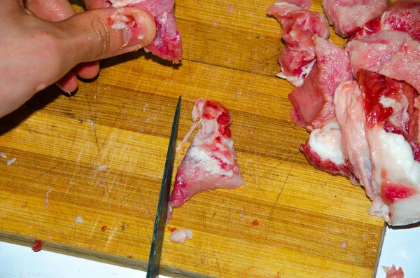 Rått kött på tavlan. En man skär fläskkött i bitar med kniv. Kött med bacon. Sjukdomar i rått kött. Feta händer från kött — Stockfoto