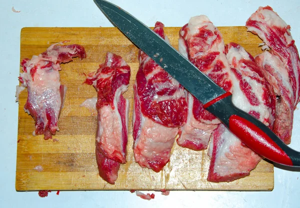 Raw meat on the board. A man cuts pork meat into pieces with a knife. Meat with bacon. Diseases of raw meat. Fat hands from meat — ストック写真