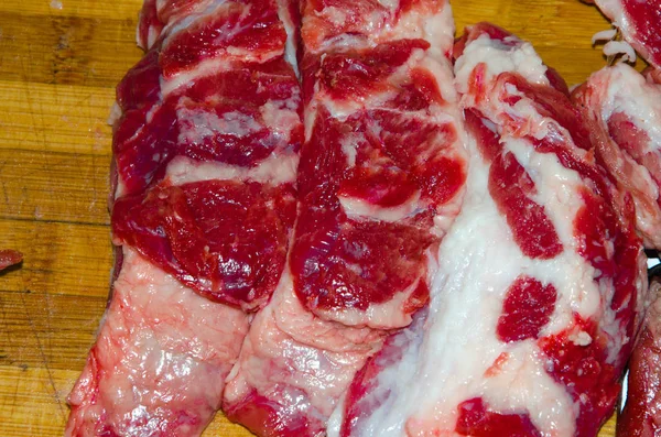 Surowe mięso na desce. Mężczyzna kroi mięso wieprzowe na kawałki nożem. Mięso z bekonem. Choroby surowego mięsa. Tłuste ręce z mięsa — Zdjęcie stockowe