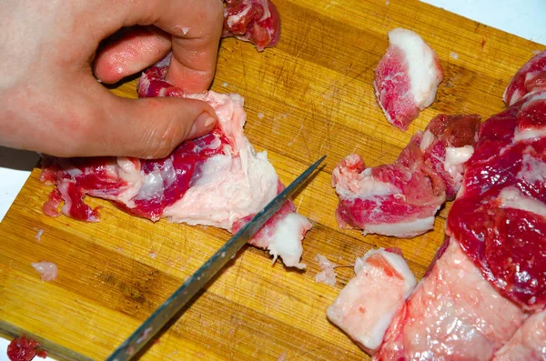Carne cruda en el tablero. Un hombre corta carne de cerdo en pedazos con un cuchillo. Carne con tocino. Enfermedades de la carne cruda. Las manos gordas de la carne — Foto de Stock