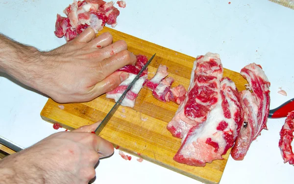Raw meat on the board. A man cuts pork meat into pieces with a knife. Meat with bacon. Diseases of raw meat. Fat hands from meat — 스톡 사진