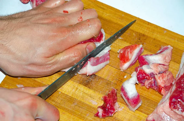 Raw meat on the board. A man cuts pork meat into pieces with a knife. Meat with bacon. Diseases of raw meat. Fat hands from meat — Stock Photo, Image