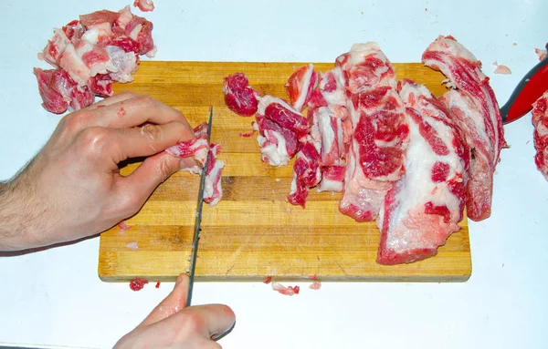 Carne cruda en el tablero. Un hombre corta carne de cerdo en pedazos con un cuchillo. Carne con tocino. Enfermedades de la carne cruda. Las manos gordas de la carne — Foto de Stock