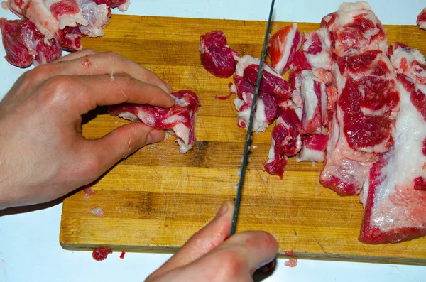 Rått kött på tavlan. En man skär fläskkött i bitar med kniv. Kött med bacon. Sjukdomar i rått kött. Feta händer från kött — Stockfoto