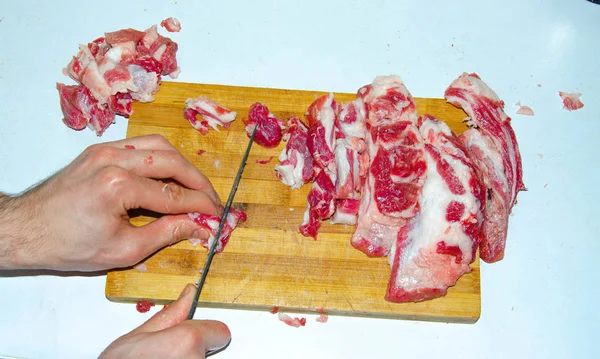 Rått kött på tavlan. En man skär fläskkött i bitar med kniv. Kött med bacon. Sjukdomar i rått kött. Feta händer från kött — Stockfoto