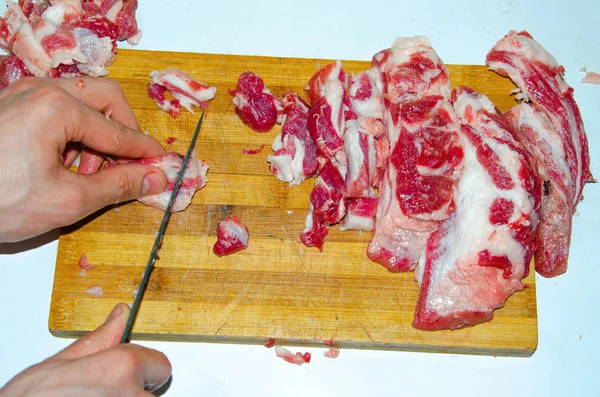 Carne crua no tabuleiro. Um homem corta carne de porco em pedaços com uma faca. Carne com bacon. Doenças de carne crua. Mãos gordas de carne — Fotografia de Stock