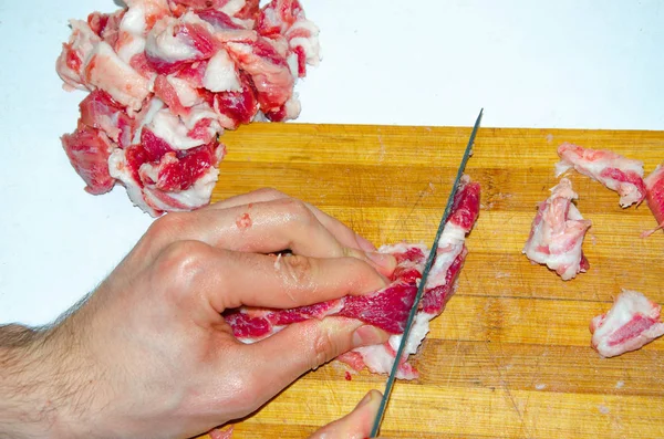 Carne crua no tabuleiro. Um homem corta carne de porco em pedaços com uma faca. Carne com bacon. Doenças de carne crua. Mãos gordas de carne — Fotografia de Stock