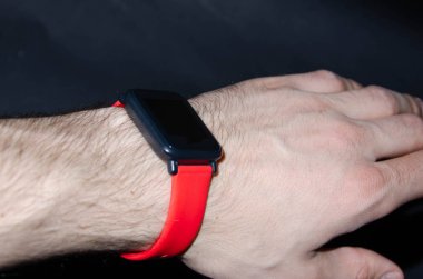 Kırmızı kayışlı akıllı saat. Elinde parlak bir kayış ve siyah bir arka planla akıllı bir saat. Spor aktivitelerini izliyorum. Spor yapmak