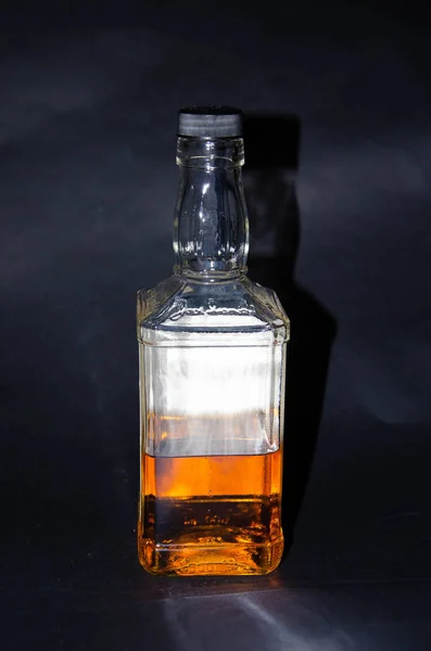 Botella de whisky medio llena sobre fondo negro. Una botella en la mano de un hombre. Whisky de malta. Alcohol. Una botella de whisky desde diferentes ángulos. Botella inferior, cuello con tapa. Adicción al alcohol — Foto de Stock