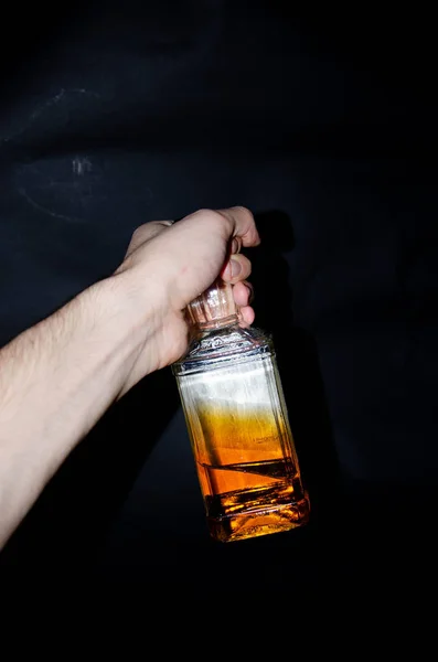 Bottiglia di whisky mezza piena su fondo nero. Una bottiglia nella mano di un uomo. Whisky single malt. Alcol. Una bottiglia di whisky da diverse angolazioni. Fondo bottiglia, collo con tappo. Dipendenza da alcol — Foto Stock
