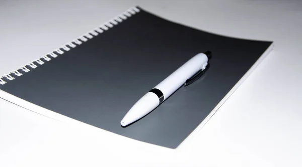 Šedý zápisník s bílým perem na bílém pozadí. Zápisník na poznámky, nápady, úkoly. Deník. — Stock fotografie
