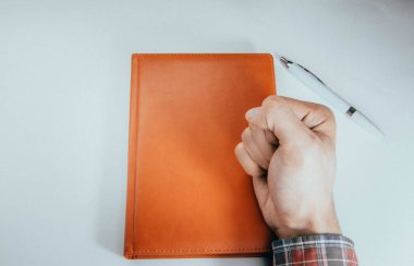 Erkek eli, ön kol kalem, defter, akıllı telefon. Eller deftere hücre fikirleriyle, planlarıyla, görevleriyle yazarlar. Defteri tekmele, kır, bük. Copyspace Kopya Space Orange, günlük. Görevlerle çalış. 