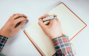 Erkek eli, ön kol kalem, defter, akıllı telefon. Eller deftere hücre fikirleriyle, planlarıyla, görevleriyle yazarlar. Defteri tekmele, kır, bük. Copyspace Kopya Space Orange, günlük. Görevlerle çalış.