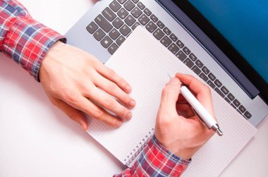 Kareli gömlekli bir adamın elleri beyaz bir kalem tutar ve bir deftere yazar. El yazıları, fikirler, notlar, not defterine görev planları. Serbest yazar, programcı. Bilgisayarda çalış.