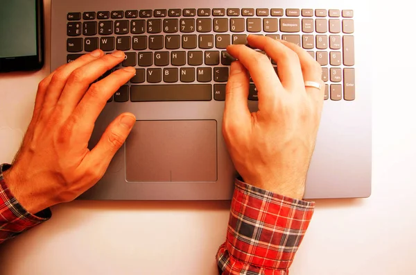 Men\'s hands in a shirt in a cage lie on the keyboard on a laptop from a first-person view from above. Hands are typing on a laptop. Freelancer, programmer. Typing in the blind. Work at the laptop