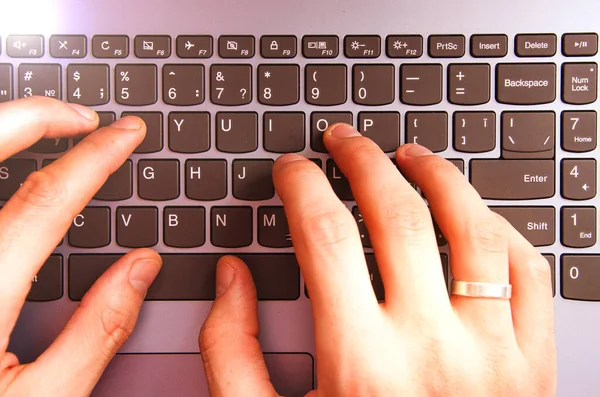 Men\'s hands in a shirt in a cage lie on the keyboard on a laptop from a first-person view from above. Hands are typing on a laptop. Freelancer, programmer. Typing in the blind. Work at the laptop