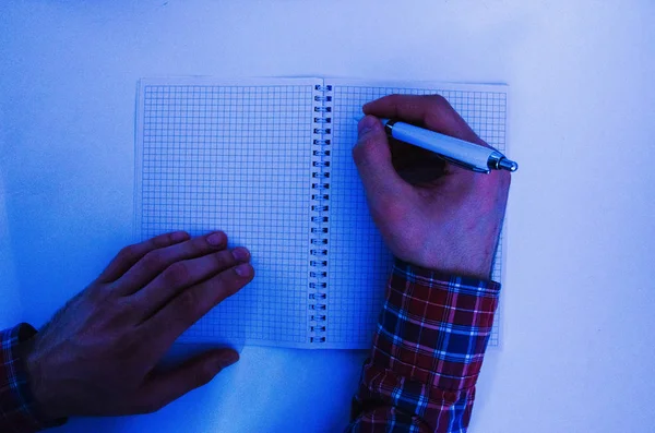 小切手のシャツを着た男性の手は白いペンを持ち ノートに書き込みます ノートブックにアイデア タスク計画を入力する手 フリーランス プログラマー ノートパソコンで働く — ストック写真