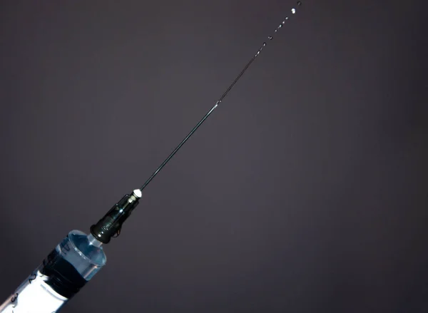 Syringe with a needle on a gray dark background. A drop, a stream flows from a syringe needle. Macro