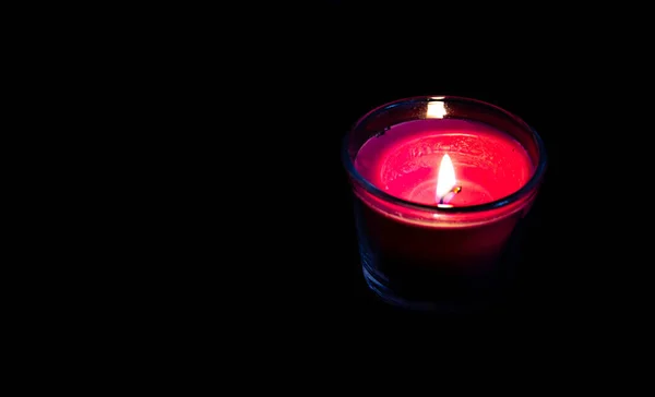 Bright pink candle in a glass jar on a black background. The candle is burning. Extinguished candle. Smoke from the candle. Hearth of fire. Tongue of flame. Macro.