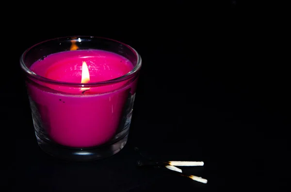 Bright pink candle in a glass jar on a black background. The candle is burning. Extinguished candle. Smoke from the candle. Hearth of fire. Tongue of flame. Macro.