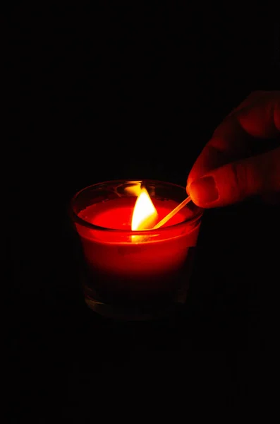 Bright pink candle in a glass jar on a black background. The candle is burning. Redeemed. A hand sets fire to a candle with matches. Put out the candle with your fingers, hands.