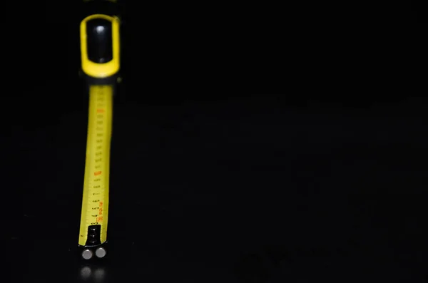 Construction bright yellow tape measure on a black background from the side, front. Place for the name of the inscriptions on the tape measure.