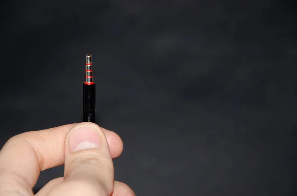 Jack 3.5mm in hand on a black background in macro. Headphone jack black with red pins