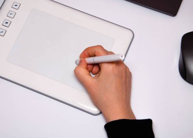 Kadın elleri grafik tablet üzerinde çalışır. El, stil kalemi tutuyor ve çiziyor. Beyaz grafik tablet. Bir grafik tasarımcısının işi. Kız bilgisayara bağlı bir tablet üzerinde çalışıyor. Arkadan görünüm